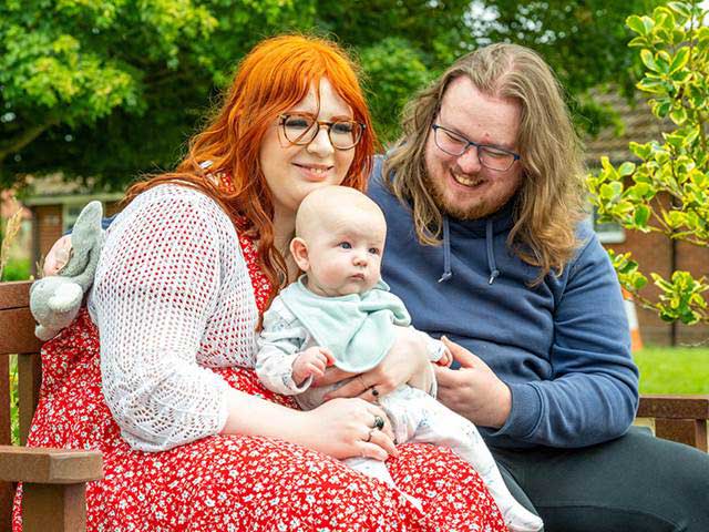 Family with baby sat on park bench